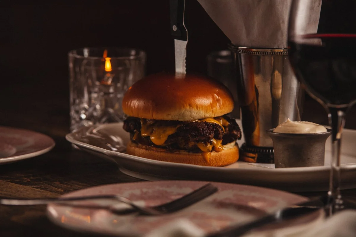 A cheeseburger on a glossy bun with a steak knife through the top.
