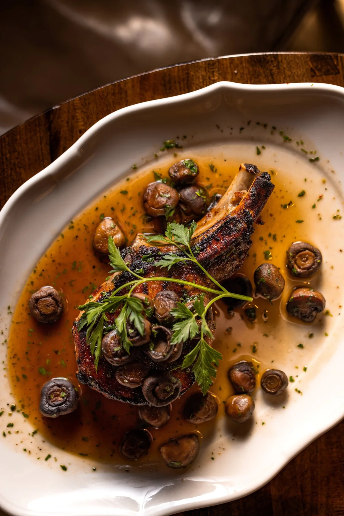 A bone-in chop in pan sauce with button mushrooms and parsley.