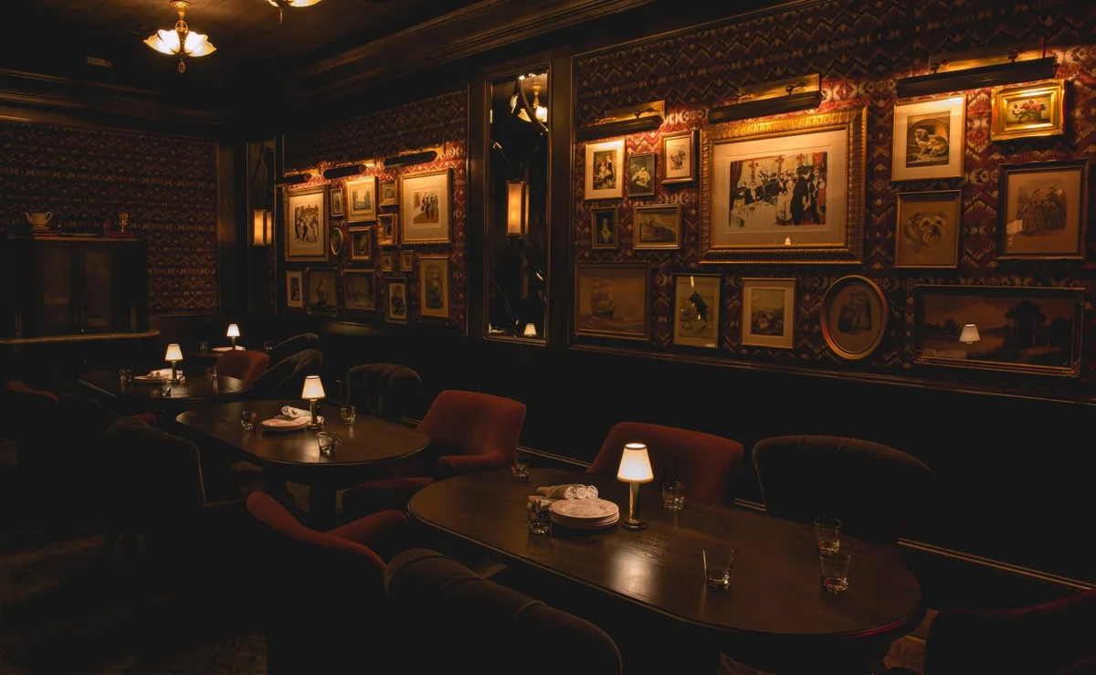 The dining room: oval tables with lamps and velvet chairs under a wall of framed pictures.