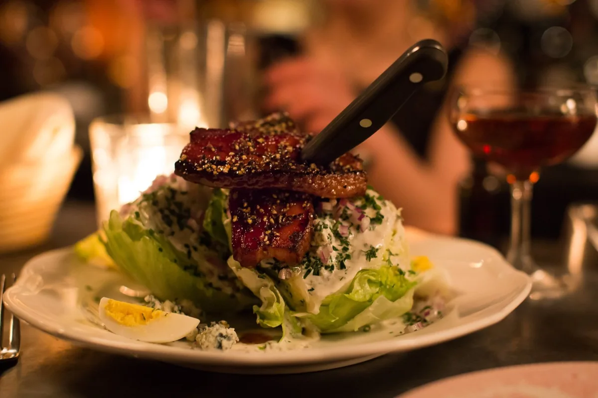 A wedge salad under thick-cut peppered bacon, a steak knife standing in it.